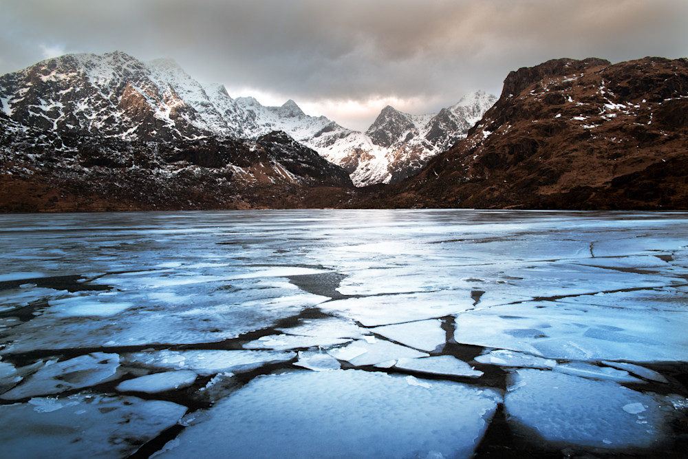 The sun breaks through for just a moment on a moody winter day in the Lofoten Archipelago over an icy lake, norway