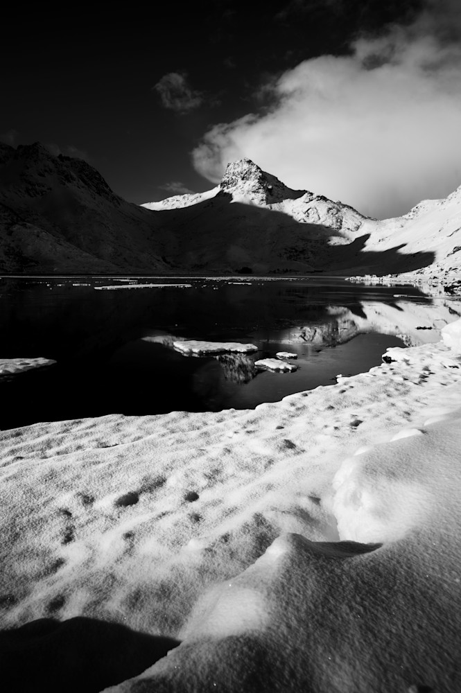 A mountain is reflected in a dead calm lake in Vestvågøy, Norway in the Lofoten Islands as a black and white image