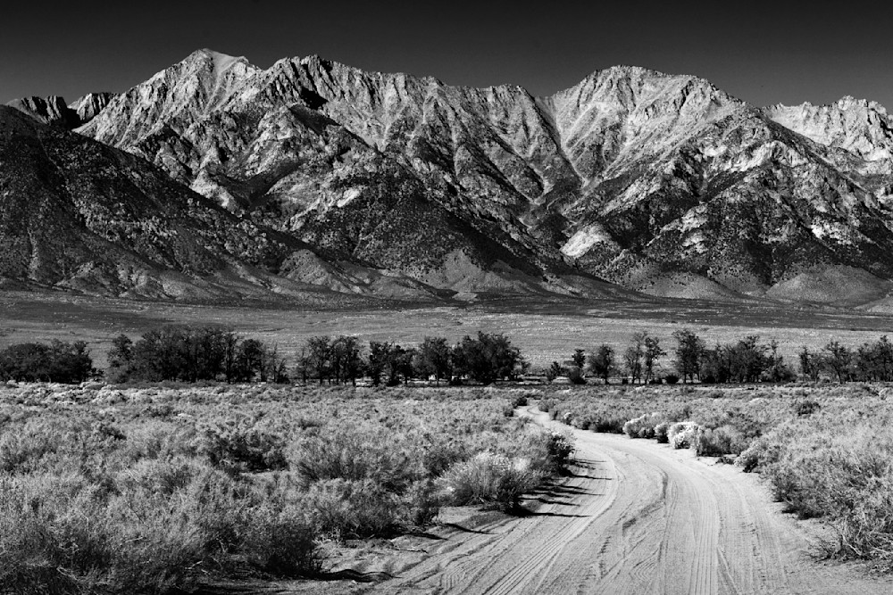Black and white high resolution photo of desert valley road leading to snow capped Sierra Nevada Mountains