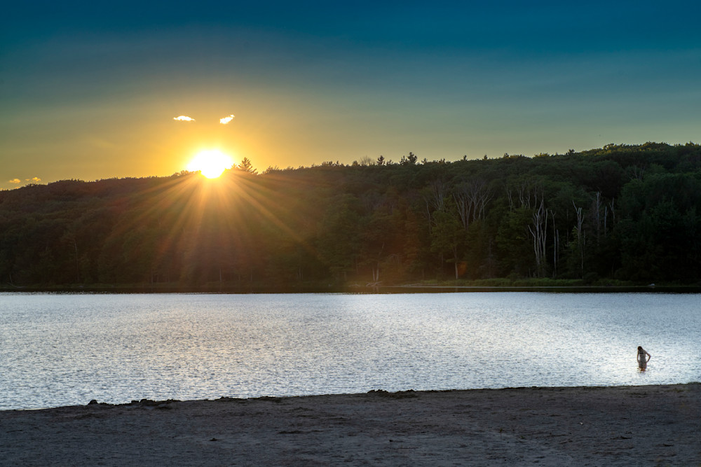 sun setting behind mountain lake with lone swimmer in foreground