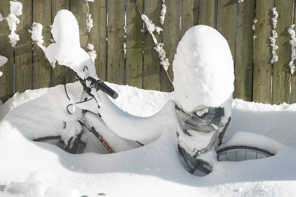 Bicycle covered in snow, with snow piled high upon seat and handlebars