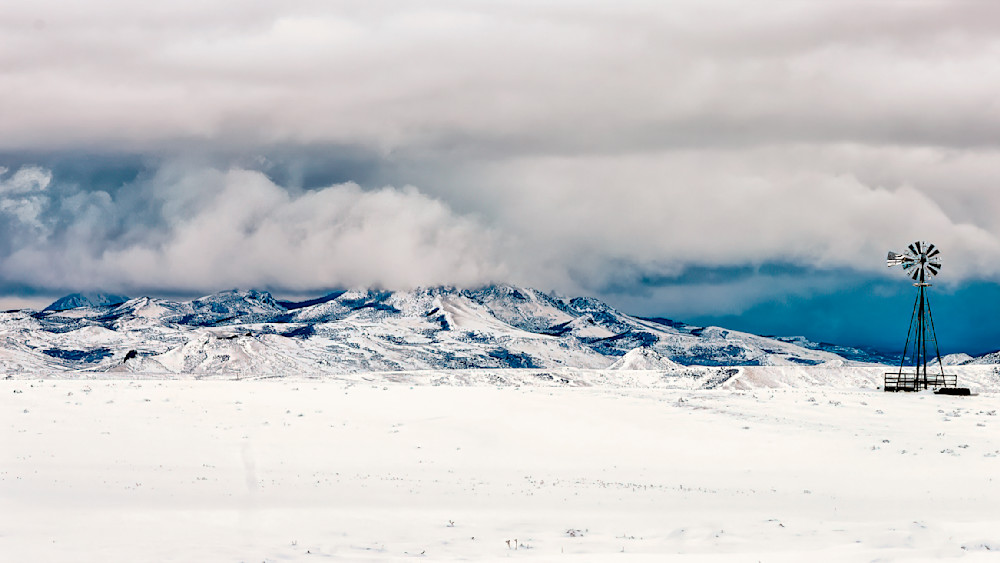 Windmill stands tall against approaching storm clouds on the snowy State Line plains