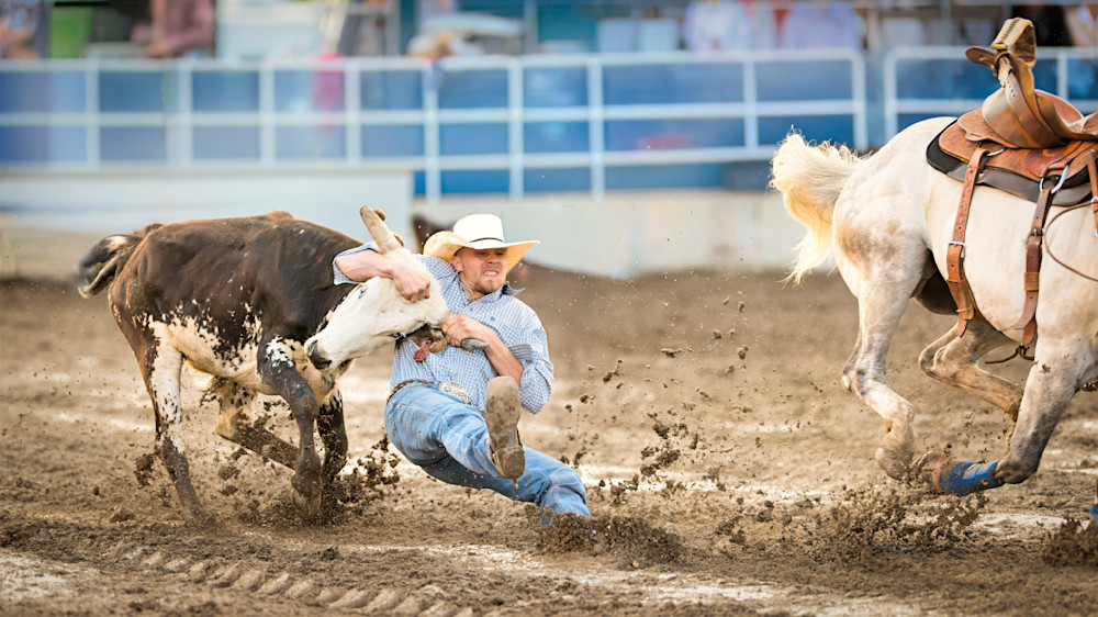 Cowboy capturing a calf at a rodeo event in a dirt arena with spectators in the background