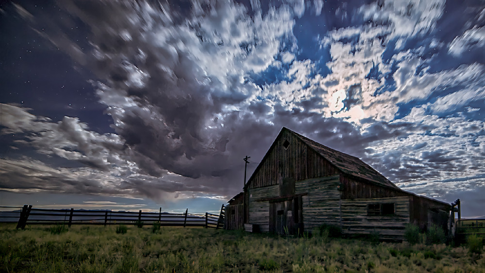Historic barn illuminated by full moon at midnight under a dramatic sky
