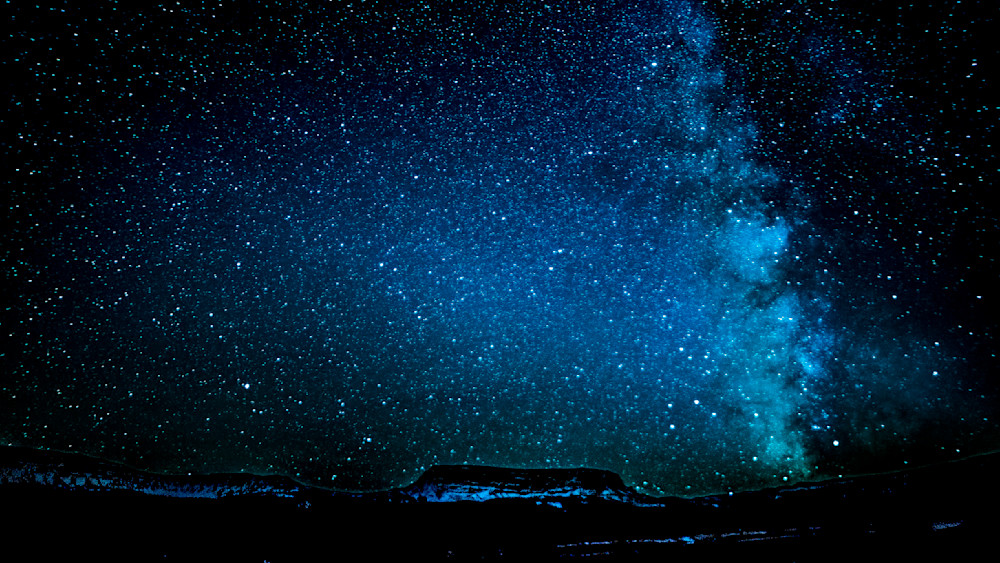 Vivid night sky filled with stars and the Milky Way over a dark landscape with mountains