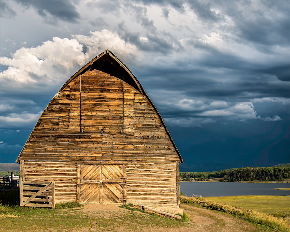 Stormy barn weather contrasts with dark clouds over a calm lake at sunset