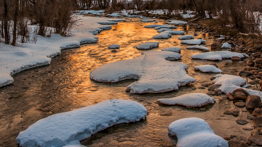 Snow caps and running water in a Rocky Mountain creek during sunset hours