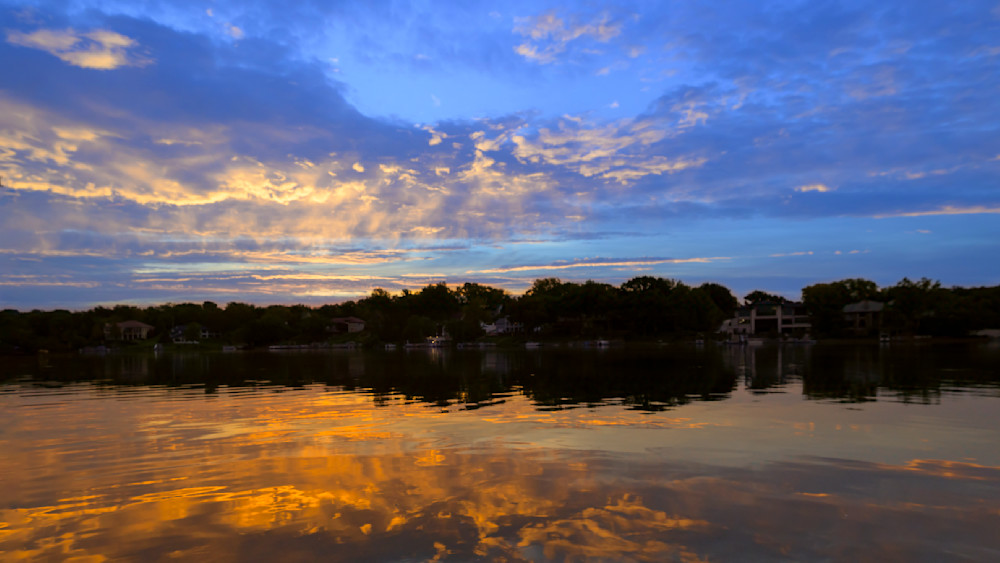 Vibrant sunrise over calm water reflecting colorful clouds in a serene lakeside setting
