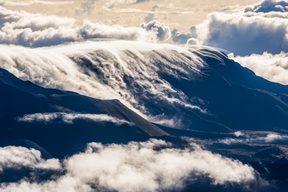Clouds flowing over Haleakala crater and surrounding mountains as seen from atop Haleakala, Maui, Hawaii, USA.