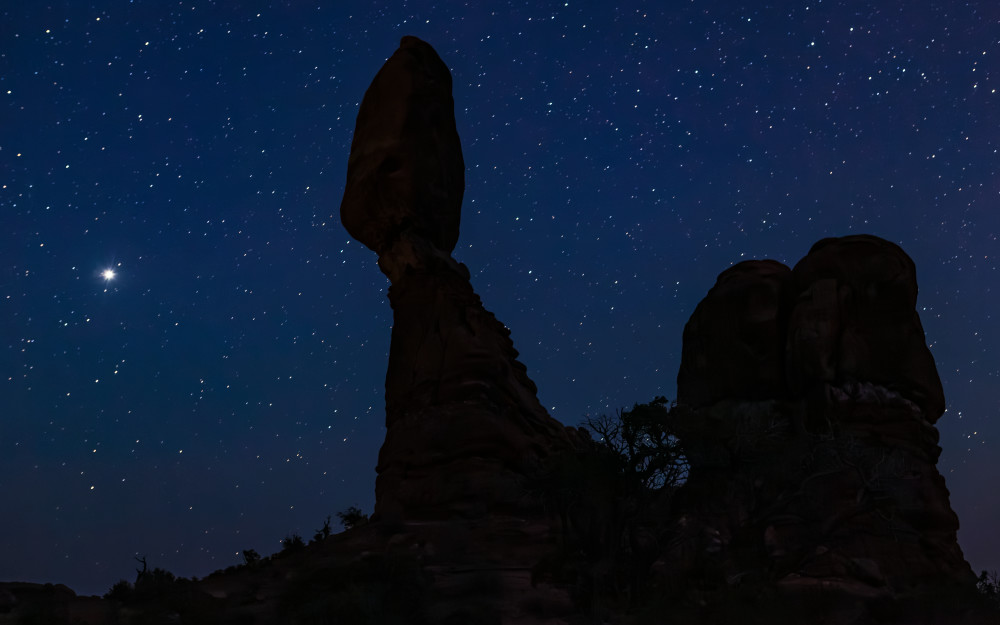 Balanced Rock in Arches National Park at night with a starry night sky in the background, Utah, USA. Jupiter shines bright on the left.