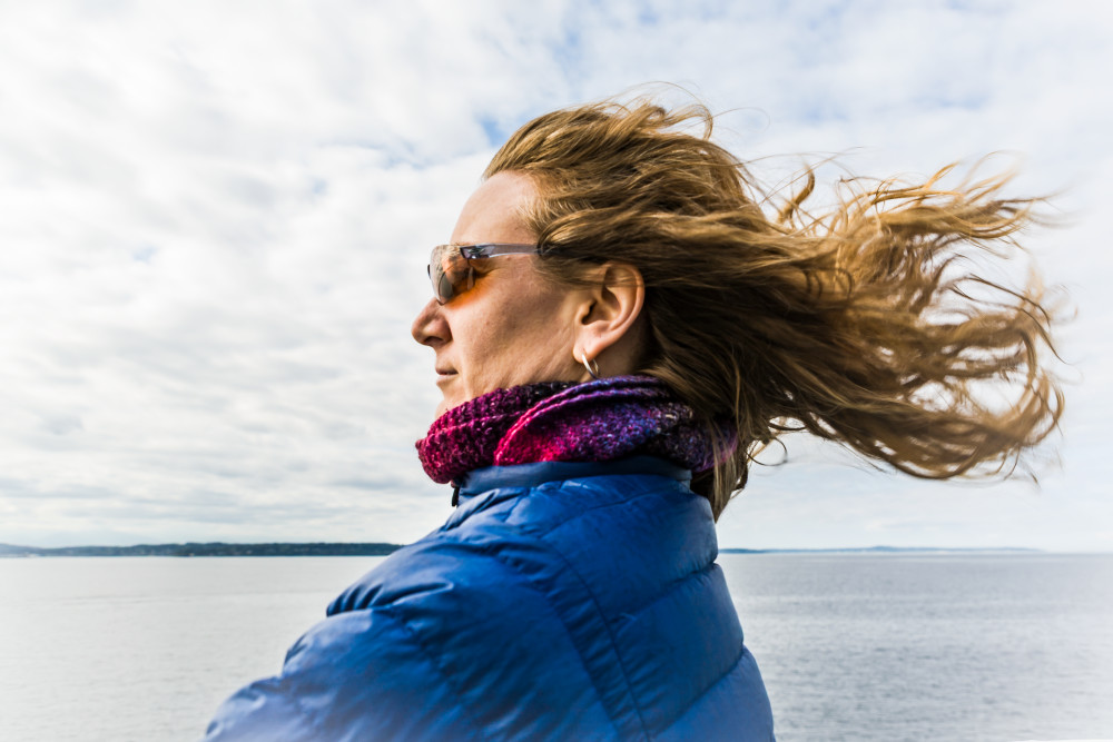 A woman with her hair waving in the wind above a body of water.