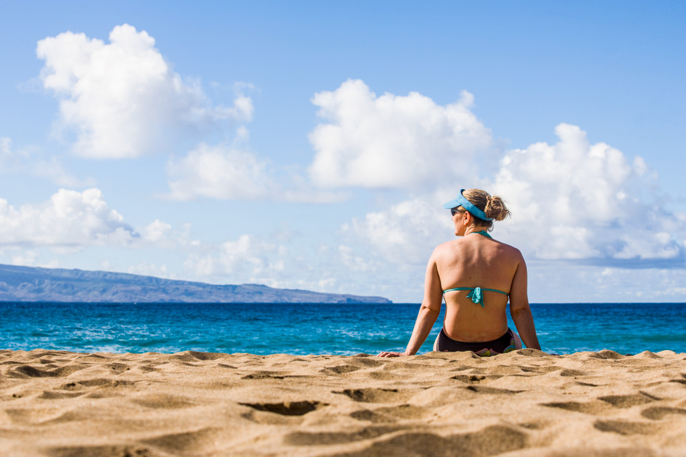 A woman relaxing on the beach enjoying the view.  Slaughterhouse Beach, Northwest Maui, Hawaii