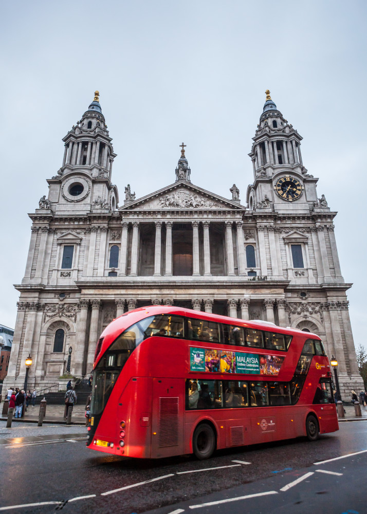 St Paul's Cathedral with an iconic red double decker bus driving by. London, UK.
