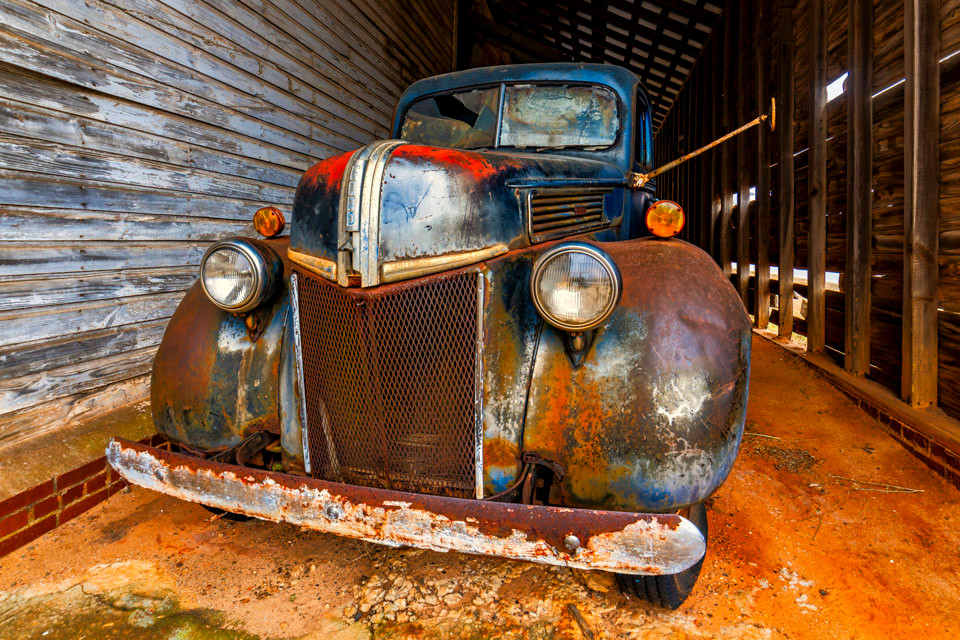 An old 1940s Ford pickup truck was tucked inside an old barn in rural Georgia. The classic pickup truck is covered in rust, but much of the original blue paint still shows through.