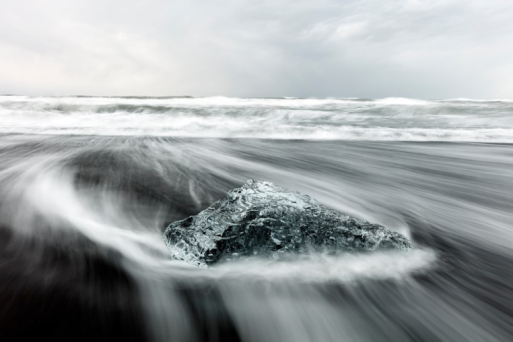 Long-exposure image of ocean water flowing around a crystal-clear iceberg on black sand beach