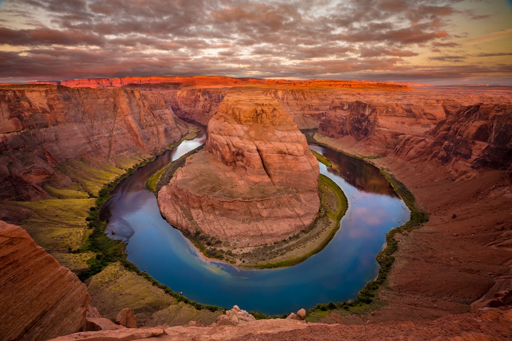 Early morning sunrise light illuminates the red rocks of Horseshoe Bend in Arizona as clouds the Colorado river flows thousands of feet below.