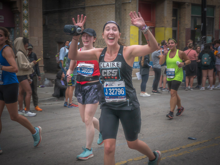 A runner at mile 21 of the Chicago Marathon with her arms up and a smile on her face