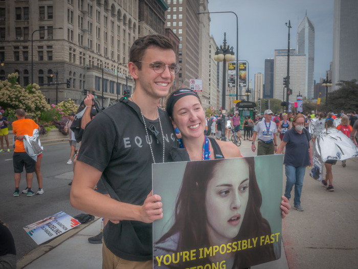 A runner and her boyfriend holding a sign at the end of the Chicago Marathon. The sign is a reference to the Twilight Series and says, "You're incredibly fast and strong."