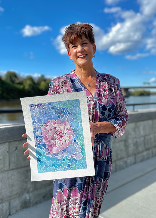 Jill Evans holding an original painting she used to design fabric for the dress she is wearing