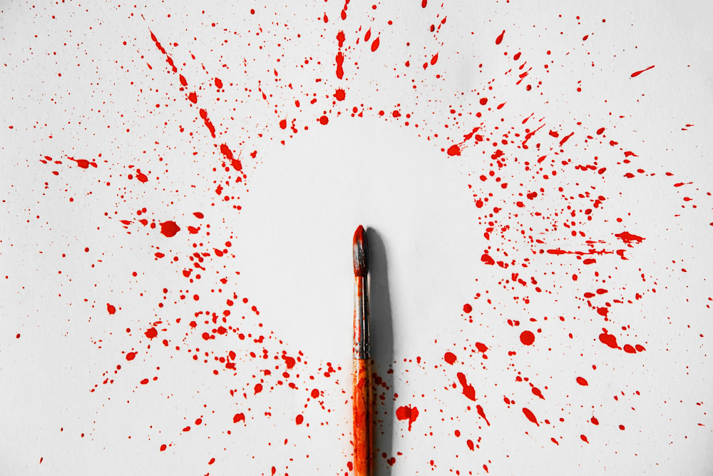 Paint brush in the middle of paint splattered on a white backrgound.