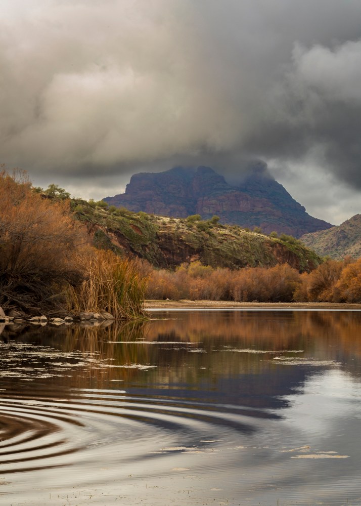 Photography wall art of the Salt River with ripples across the water’s surface and Red Mountain in the background covered in clouds.