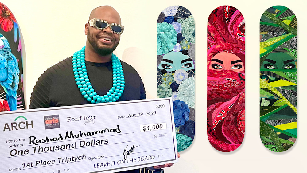 Rashad Ali Muhammad holding big first place check in front of his artwork on three skateboards