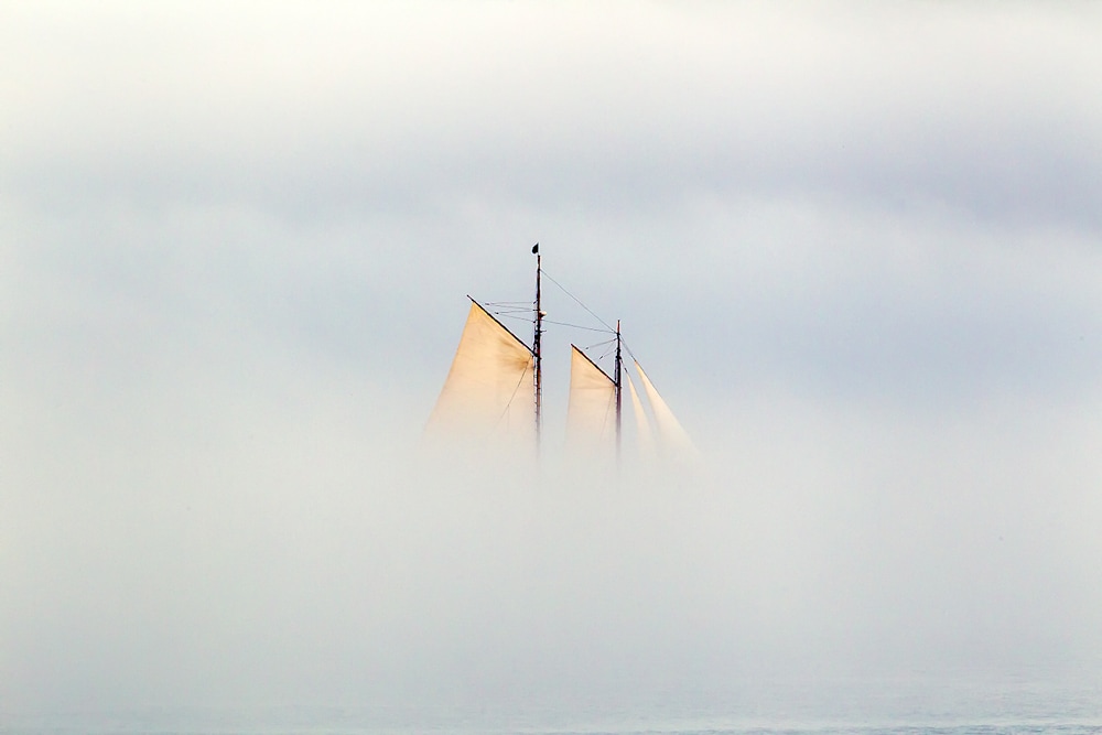 Sailboat mast and sails fading into dense ocean fog on Casco Bay, Maine