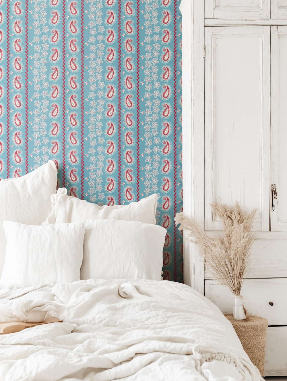 Bedroom with blue and red paisley stripe wallpaper, white bedding, and rustic white cabinet with pampas grass in a vase.