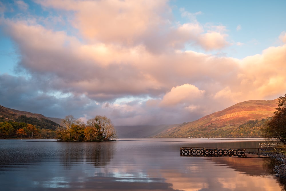 Photo of Loch Earn taken from St Fillian's at sunrise, showing blue sky with pastel-coloured clouds, and isle and a pier overlooking the loch.