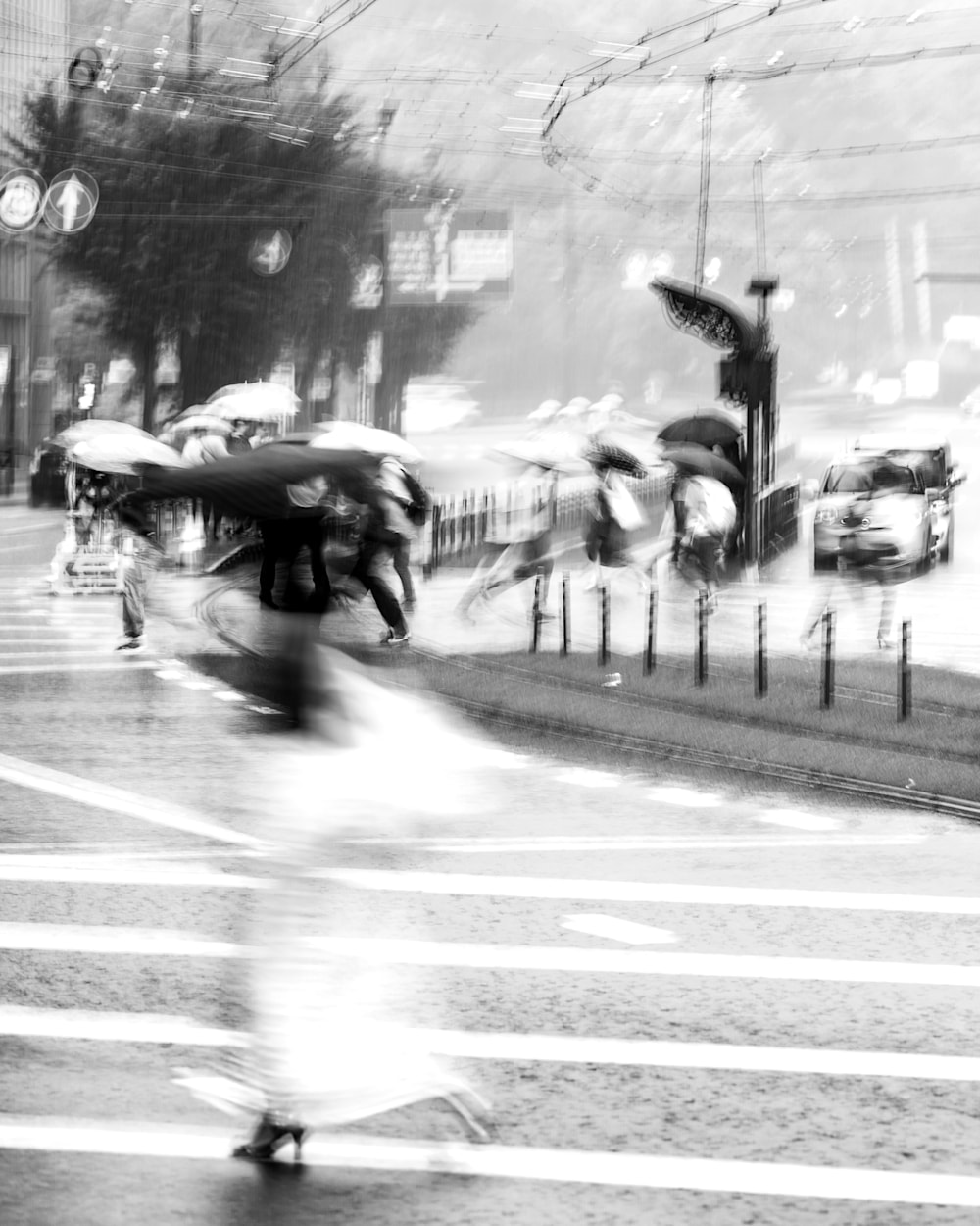 Long-exposure photograph of a woman moving through heavy rain in Kumamoto; blurred background pedestrians create the illusion of extended limbs as her umbrella arcs behind her.