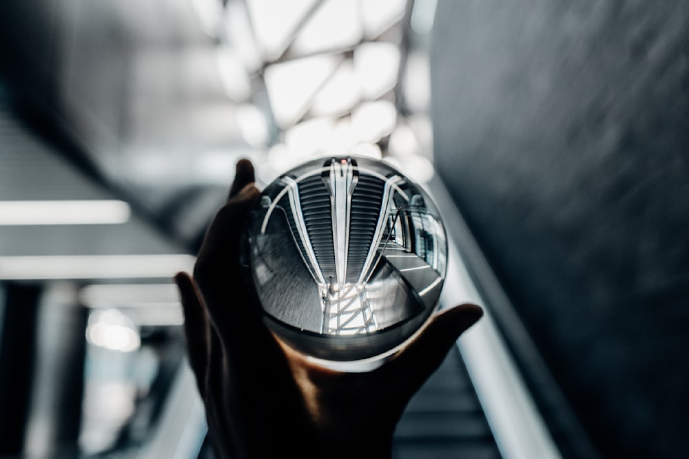 Black and white image of a hand holding a glass ball reflecting a descending  stair case- or is it ascending?