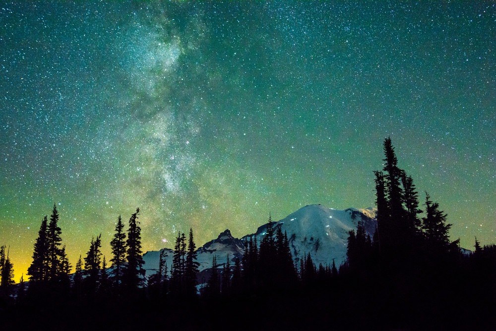 Photo of Mt. Rainier in Washington State with the milky way straight over the mountain with green night starry sky.
