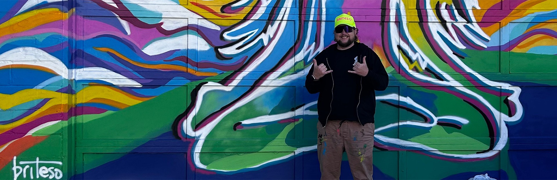 
        <div class='title'>
          Sky Mural Banner Image
        </div>
       
        <div class='description'>
          An artist stands in front of his colorfully painted mural 
        </div>
      