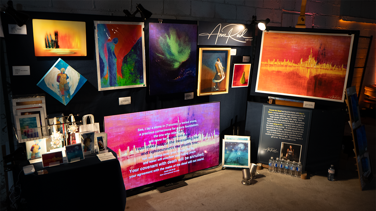 Booth view with scripture on display screen beside featured artwork